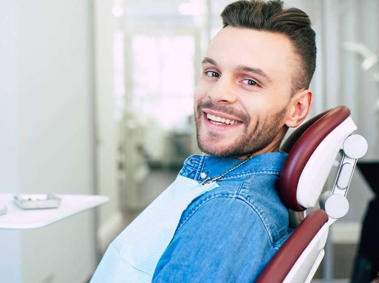 man sitting on a chair smiling before a root canal treatment in Troy NY