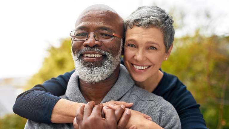 A couple smiling comfortably with their front dental crowns in Troy