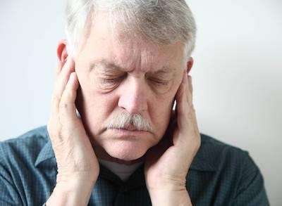 Elderly man holding his ears with a pained expression.