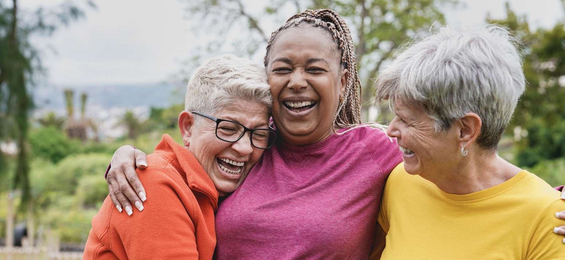 Three senior women laughing together outdoors.