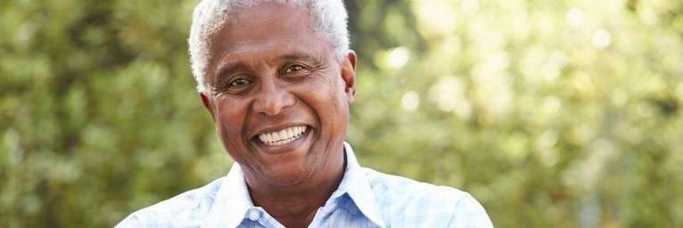 Aged man in Troy NY smiling comfortably with his complete set of teeth